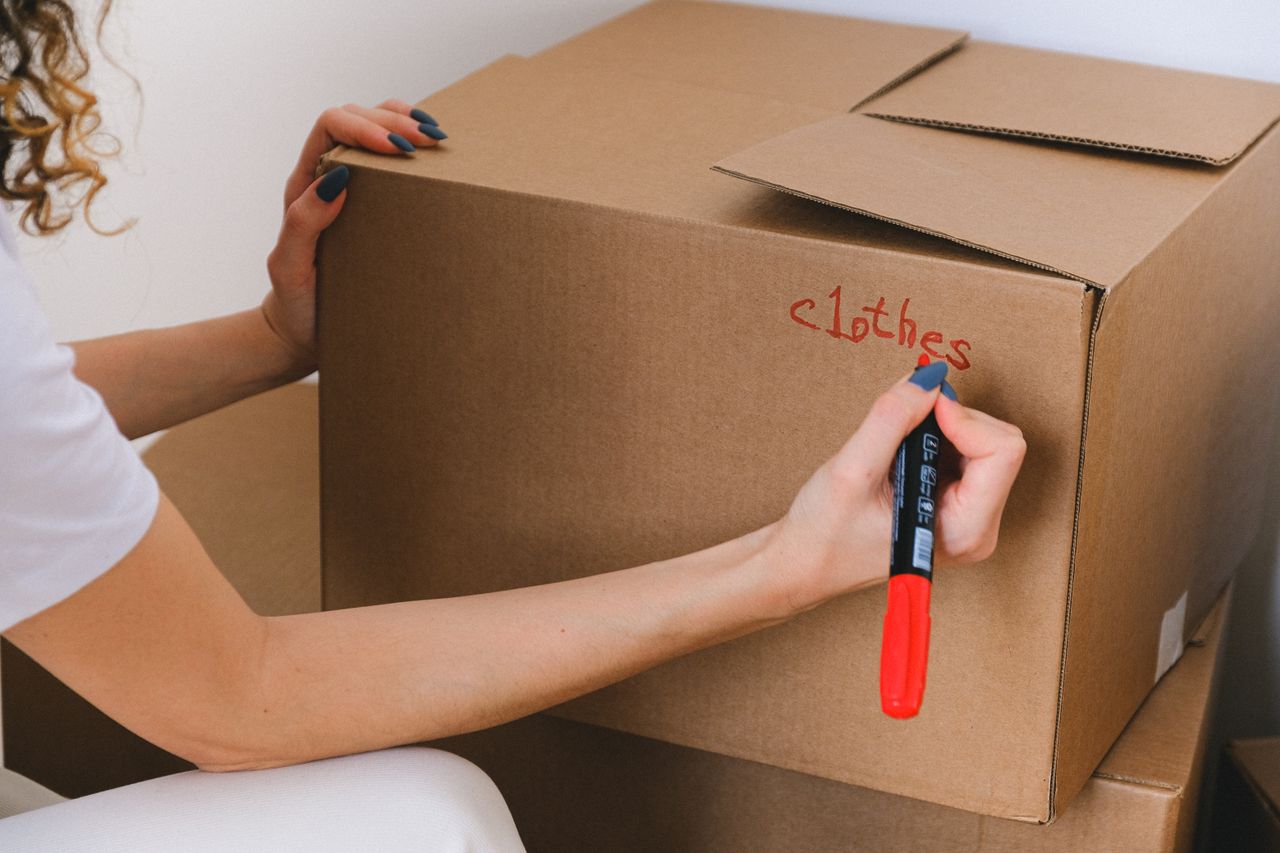 services-03 Close-up of a woman labeling a cardboard box with a red marker indoors.