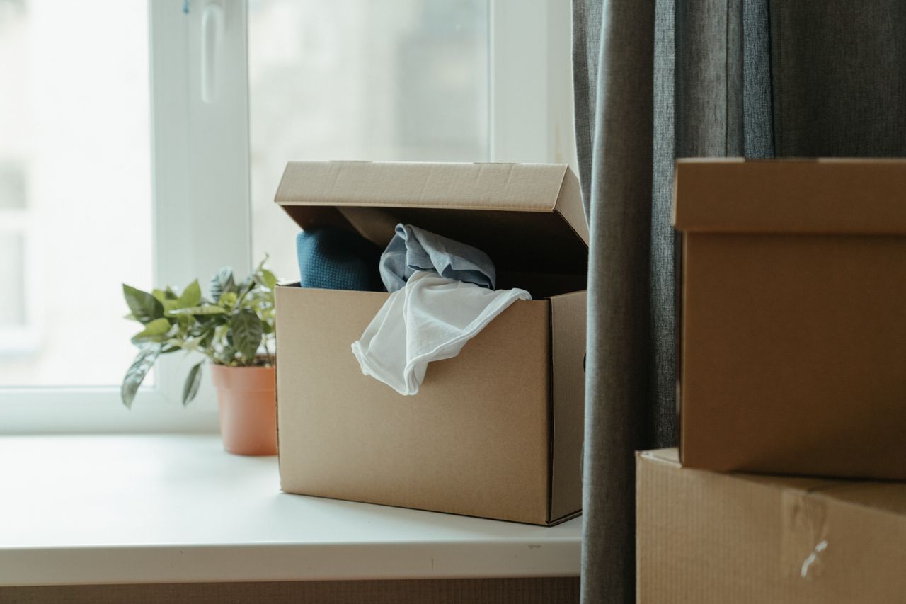 about-01 Open cardboard box with clothes by window, symbolizing moving or relocation.